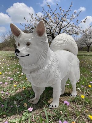 statue of a white dog standing in a field of flowers