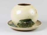 un vase blanc et vert posé sur une soucoupe, lui-même posé sur une soucoupe