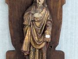 statue of a man in a robe holding a sword on a wooden plaque