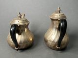 pair of silver teapots with black handles on a gray surface