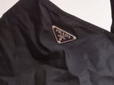 the prada bag is black and has a triangle logo on it