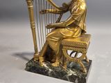 gold statue of a woman playing a harp on a marble base