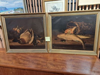 two framed paintings of fish on a wooden table in a room