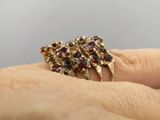 une image représentant la main d'une femme tenant une bague en or sertie d'une grenat