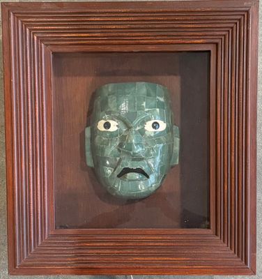 Masque en malachite verte dans un cadre en bois éclairant.