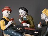 three figurines of men sitting at a table playing cards