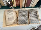 several old books are stacked on a table in front of a bookshelf