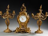 trois bougeoirs dorés et une horloge posés sur une table