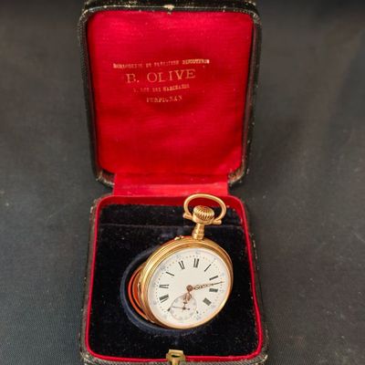 une montre de poche en or dans un écrin rouge posé sur une surface noire