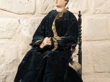 une statue représentant une femme assise sur une chaise devant un mur de pierre
