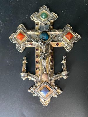 une vieille croix en argent ornée de pierres colorées, posée sur un fond noir