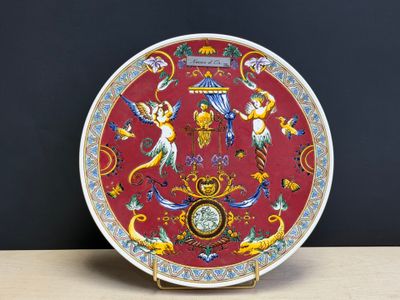 une assiette rouge sur laquelle sont représentés des anges et une horloge