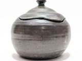 un petit vase gris muni d'un couvercle, posé sur une table