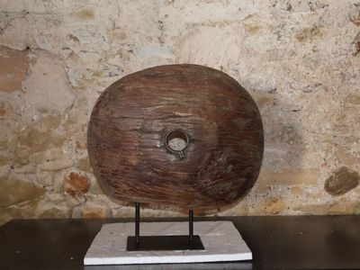 un objet en bois posé sur un socle devant un mur de pierre
