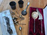une boîte contenant de l'argenterie posée sur un plancher en bois, à côté d'une paire de cuillères et de cuillères