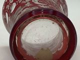 a red glass vase with holes in it on a white surface