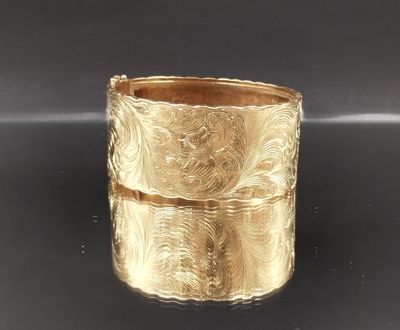 une image montrant un gros plan d'un bracelet en or posé sur une surface noire