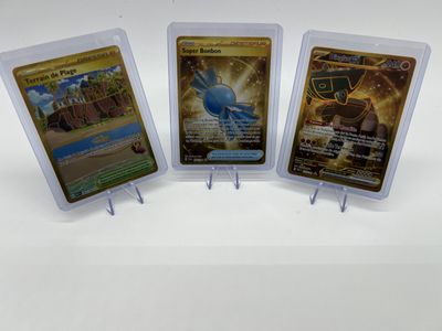 Trois cartes à collectionner Pokémon sont exposées sur une surface blanche