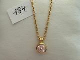 a gold necklace with a pink stone on a white pillow