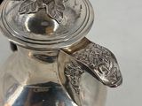 a silver tea pot with a handle on a white table