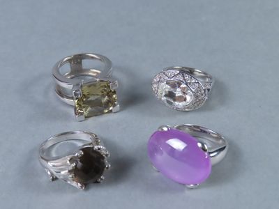 quatre bagues différentes ornées de pierres de couleurs variées sur un fond gris
