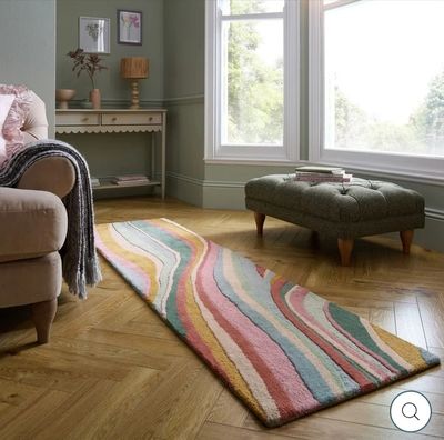 un salon avec un canapé, un fauteuil, un pouf et un tapis