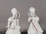deux figurines blanches représentant des femmes portant un chapeau et une canne