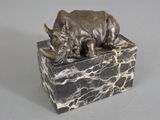 statue of a rhino resting on a marble block on a gray surface