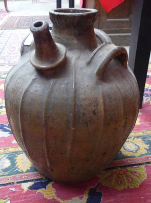 un grand vase marron posé sur un tapis coloré, à même le sol