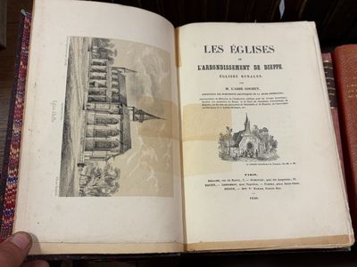 Quelqu'un tient un livre ouvert sur une table, devant une pile de livres.