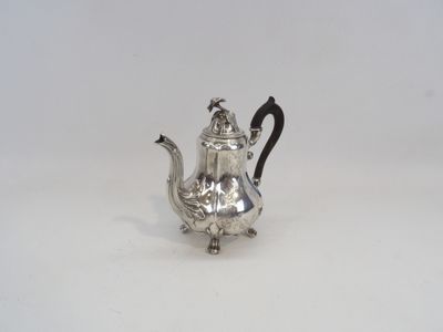 une théière ancienne en argent, dotée d'une anse noire, posée sur une surface blanche