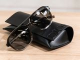 sunglasses and case on a wooden table with a white wall in the background
