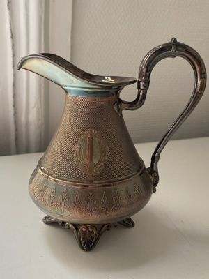 a silver pitcher sitting on a table next to a window