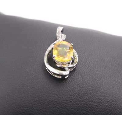 a close up of a yellow sapphire and diamond pendant on a black leather surface