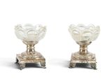 une paire de vases argentés posés sur des socles, disposés sur une surface blanche