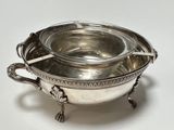 a silver bowl with a spoon in it on a white surface