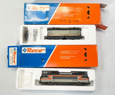 trois trains miniatures sont rangés dans des boîtes posées sur une surface blanche