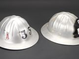 pair of silver fire hats with stickers on them sitting on a table
