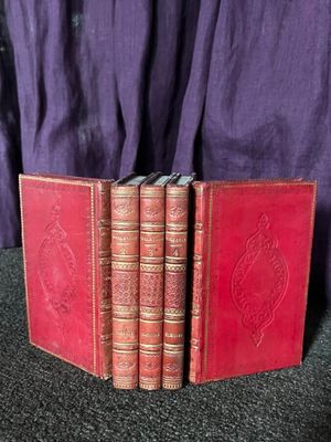 trois livres rouges posés sur une table, à côté d'un tissu violet