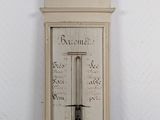 a tall white clock on the wall with a barometer on it