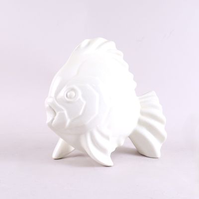 une figurine de poisson en céramique blanche posée sur une surface blanche