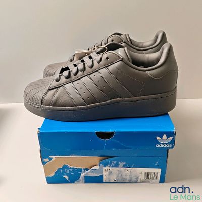 Des chaussures adidas Superstar grises et noires posées sur une boîte bleue