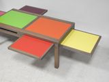 two tables with colorful tops sit on the floor in front of a white wall