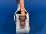 the small white bag is sitting on a blue surface with a brown strap