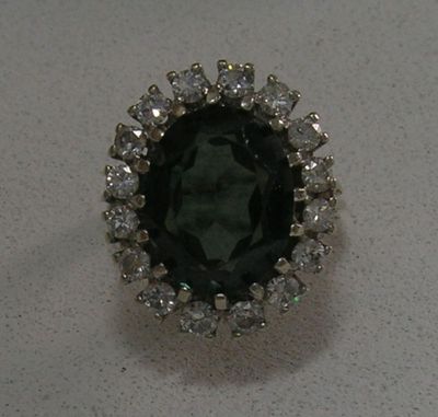 gros plan d'une bague avec une pierre verte entourée de diamants blancs