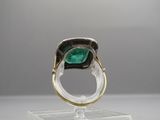 an emerald and gold ring on display on a clear surface