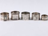 six ronds de serviette en argent, ornés de motifs variés, posés sur un fond blanc