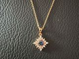 a gold necklace with a flower pendant on a black leather surface