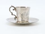 a silver cup and saucer on a saucer on a white surface
