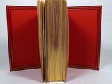 an open book sitting on top of a white table next to a red book